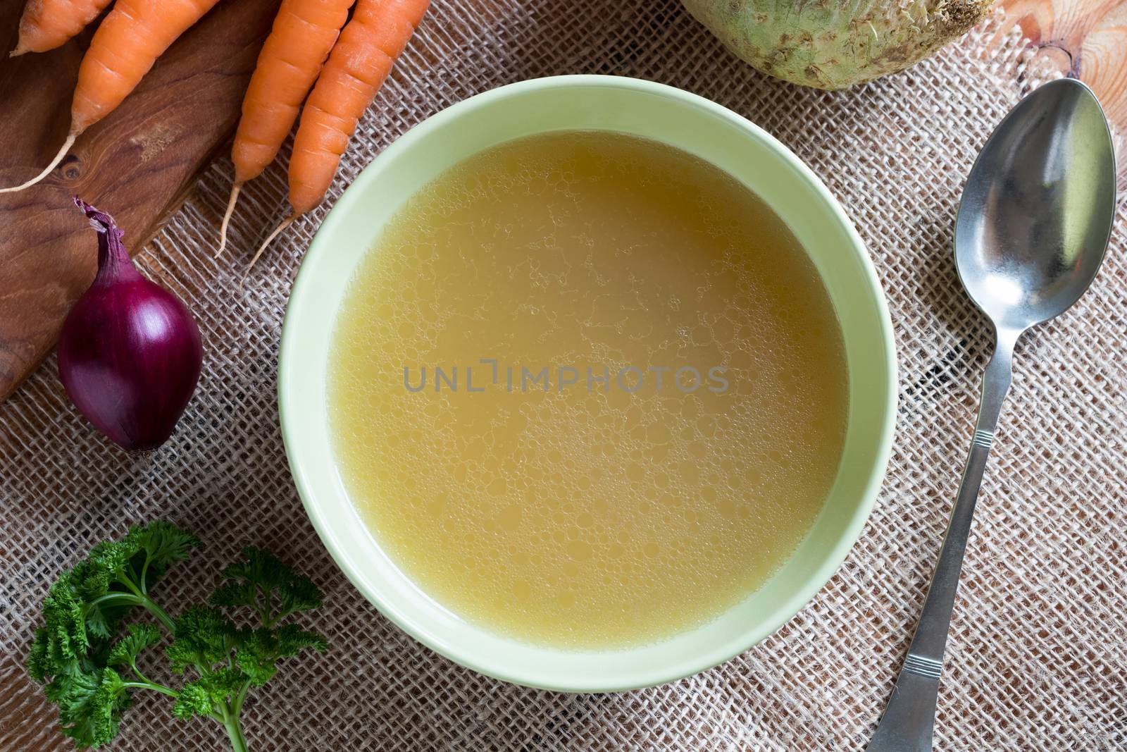 Chicken bone broth in a green soup bowl with vegetables in the background