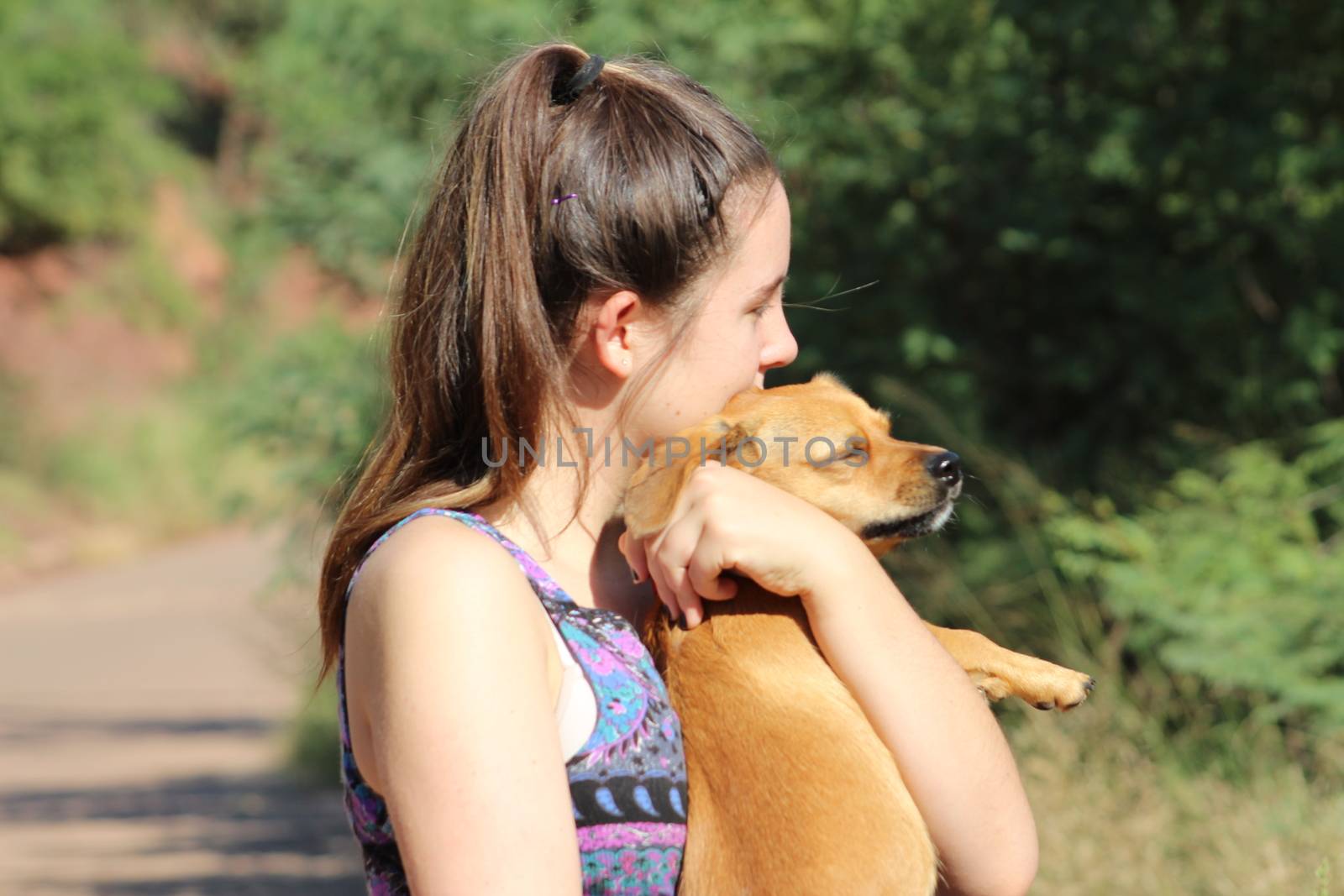 Pretty eighteen year old girl lovingly holding her little dog outside in the warm sunshine as they take a break during a long walk