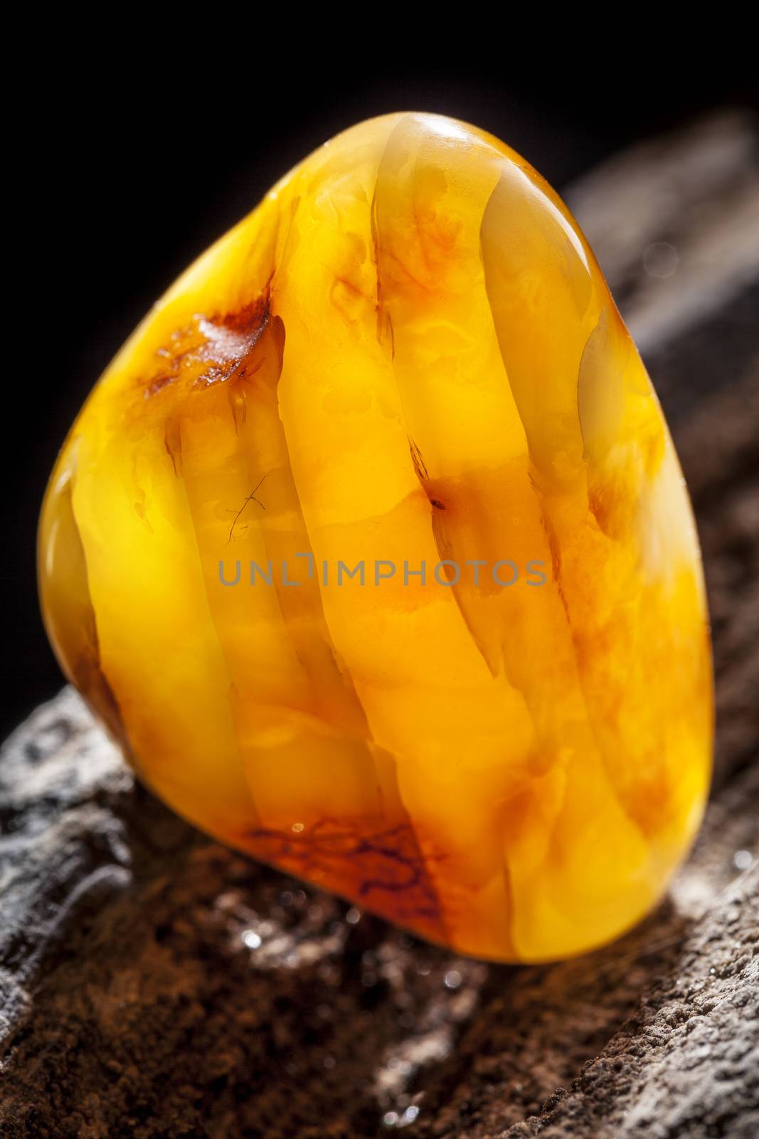 Natural amber. A piece of yellow opaque natural amber on large piece of dark stoned wood. by igor_stramyk