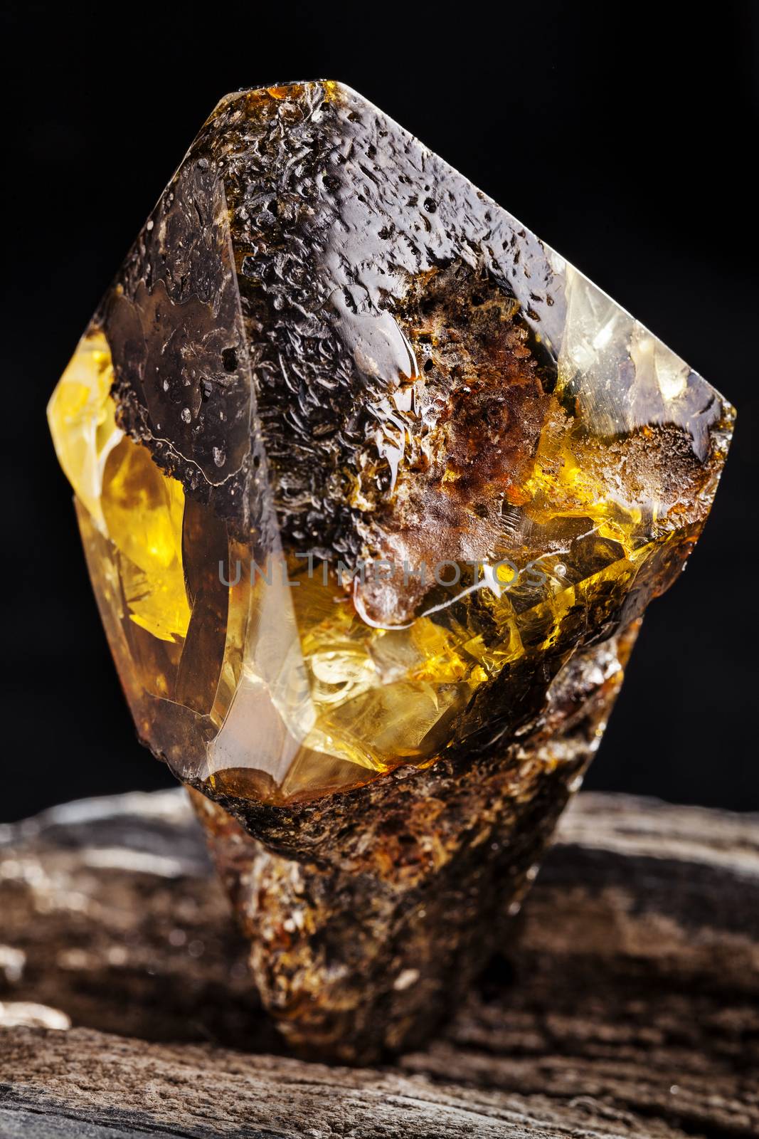 A piece of dirty amber with transparent yellow layer, has superficial cracks on its surface and many inclusions. Polished. Placed on piece of stoned wood.