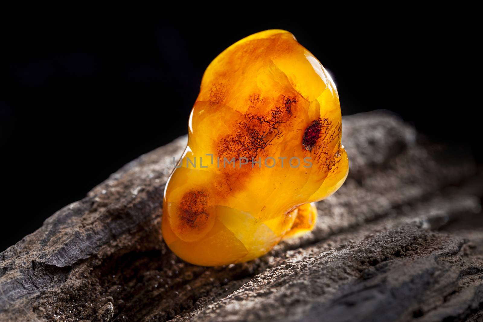 Natural amber. A piece of yellow opaque natural amber on large piece of dark stoned wood. by igor_stramyk