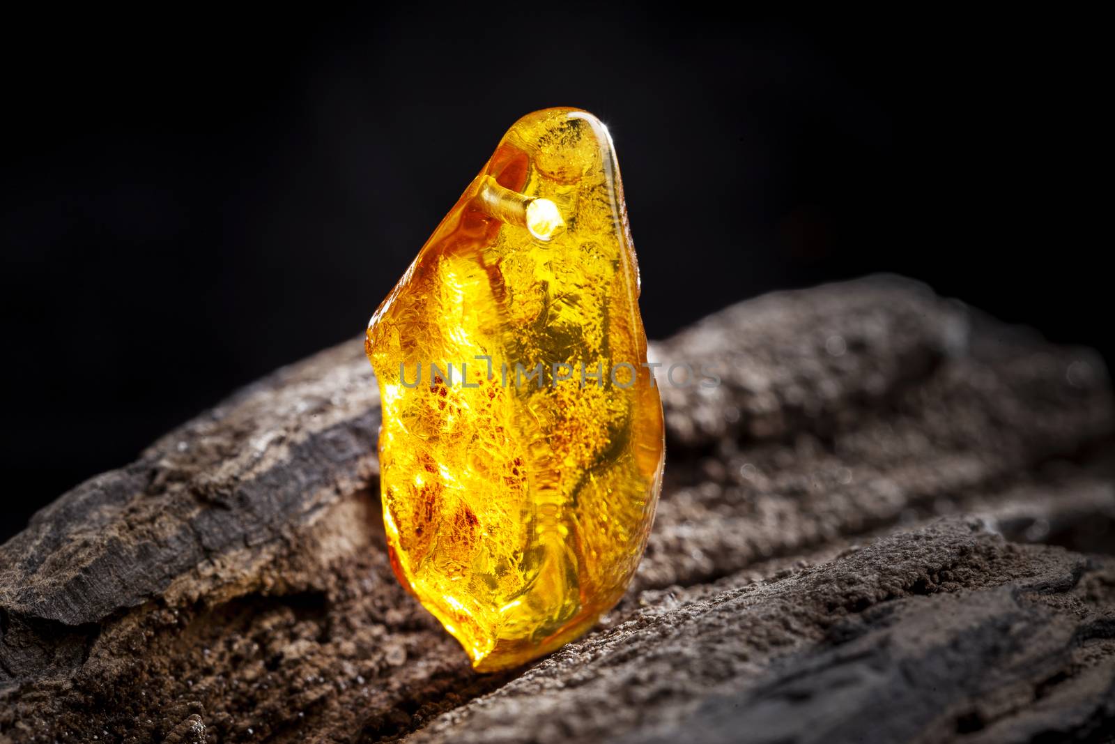Natural amber. A piece of yellow transparent natural amber on large piece of dark stoned wood. by igor_stramyk