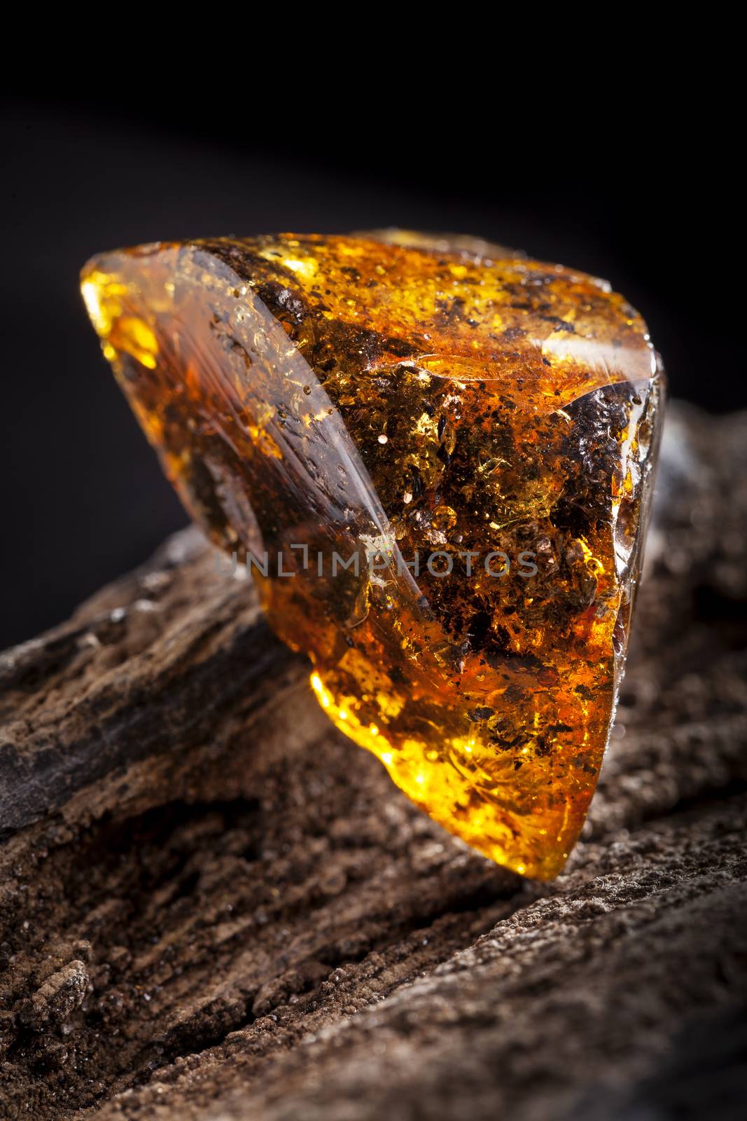 Natural amber stone. A piece of dirty transparent yellow amber on piece of stoned wood. by igor_stramyk