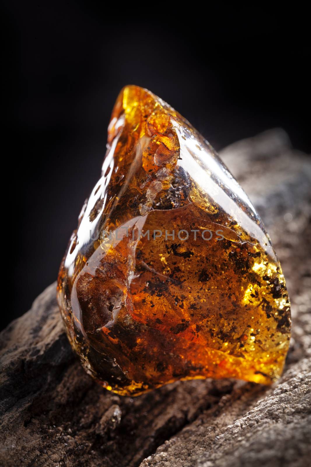 A piece of dirty yellow transparent amber, has many inclusions of natural origin. Polished. Placed on piece of stoned wood.