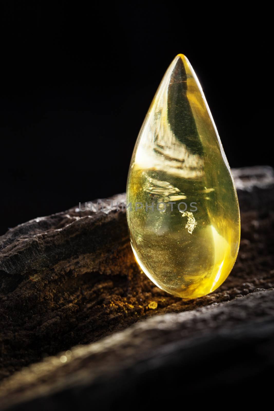 A piece of yellow clean transparent natural amber, classification color Clear Succinite, has some imprints on its surface. Polished, has partly natural shape. Placed on dark stoned wood texture.