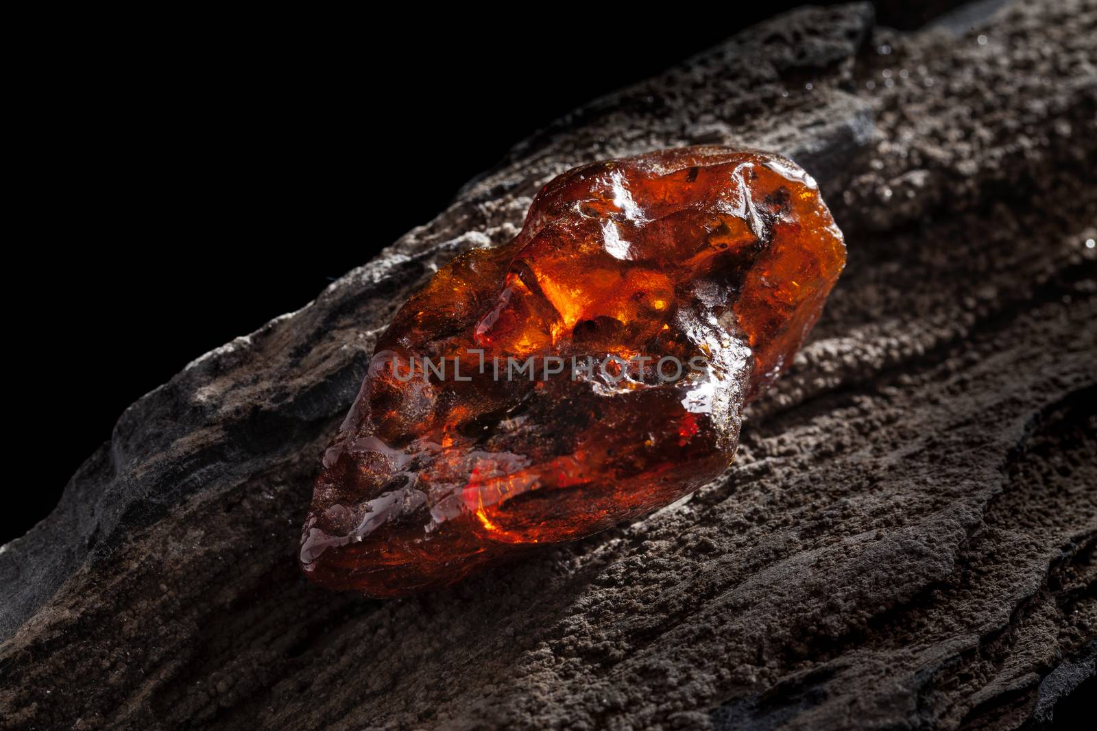 Natural amber. A piece of yellow and red semi transparent natural amber on piece of stoned wood. by igor_stramyk