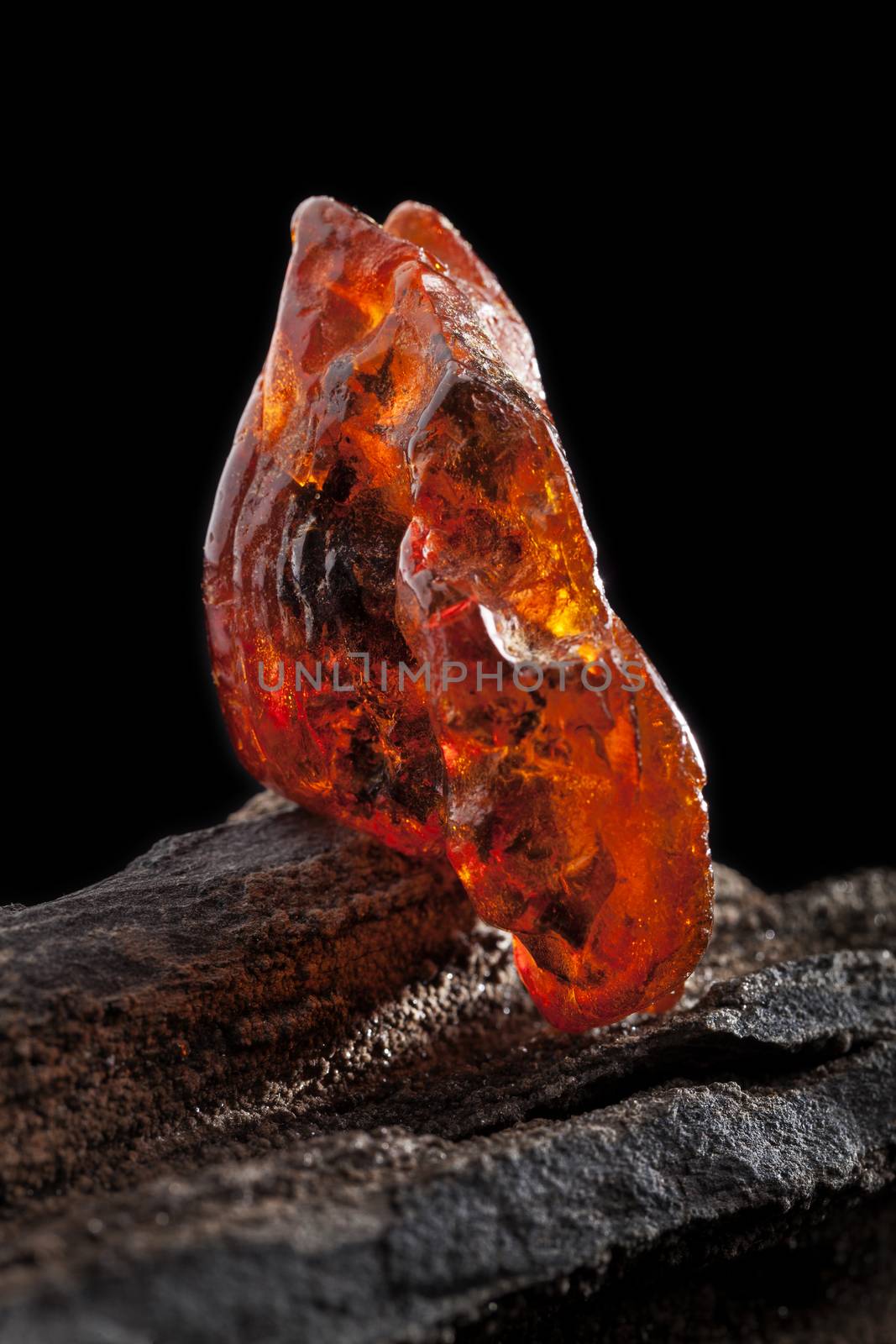 Natural amber. A piece of yellow and red semi transparent natural amber on piece of stoned wood. by igor_stramyk