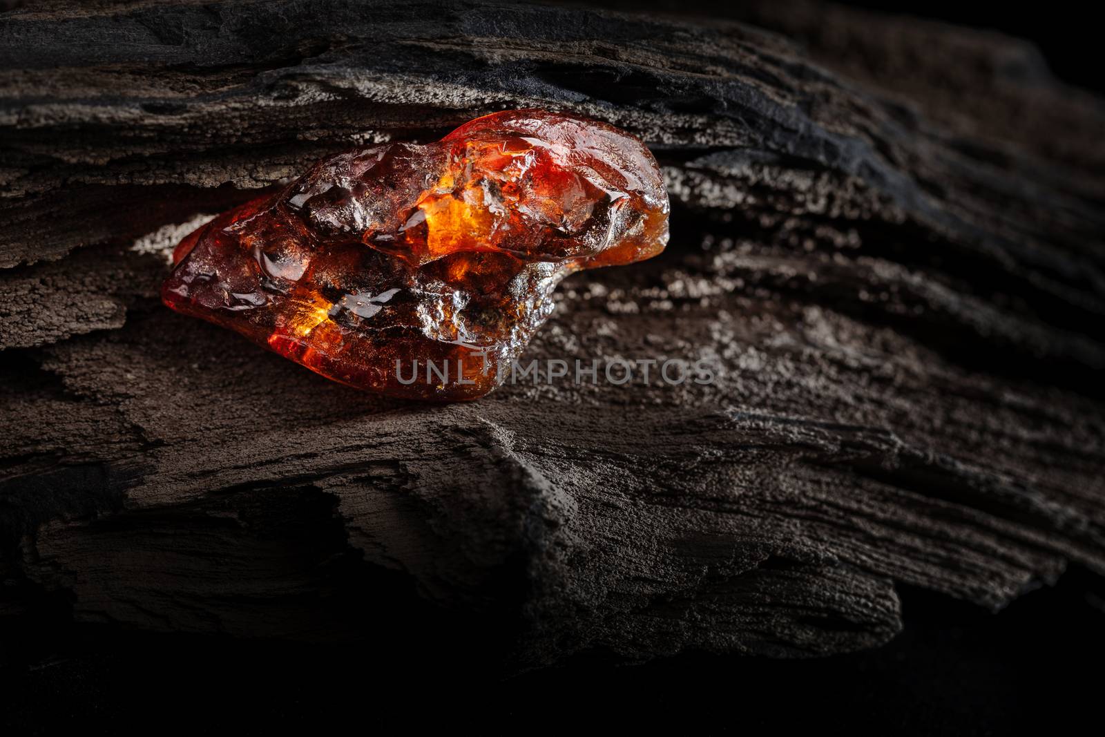 Natural amber. A piece of yellow and red semi transparent natural amber on piece of stoned wood. by igor_stramyk