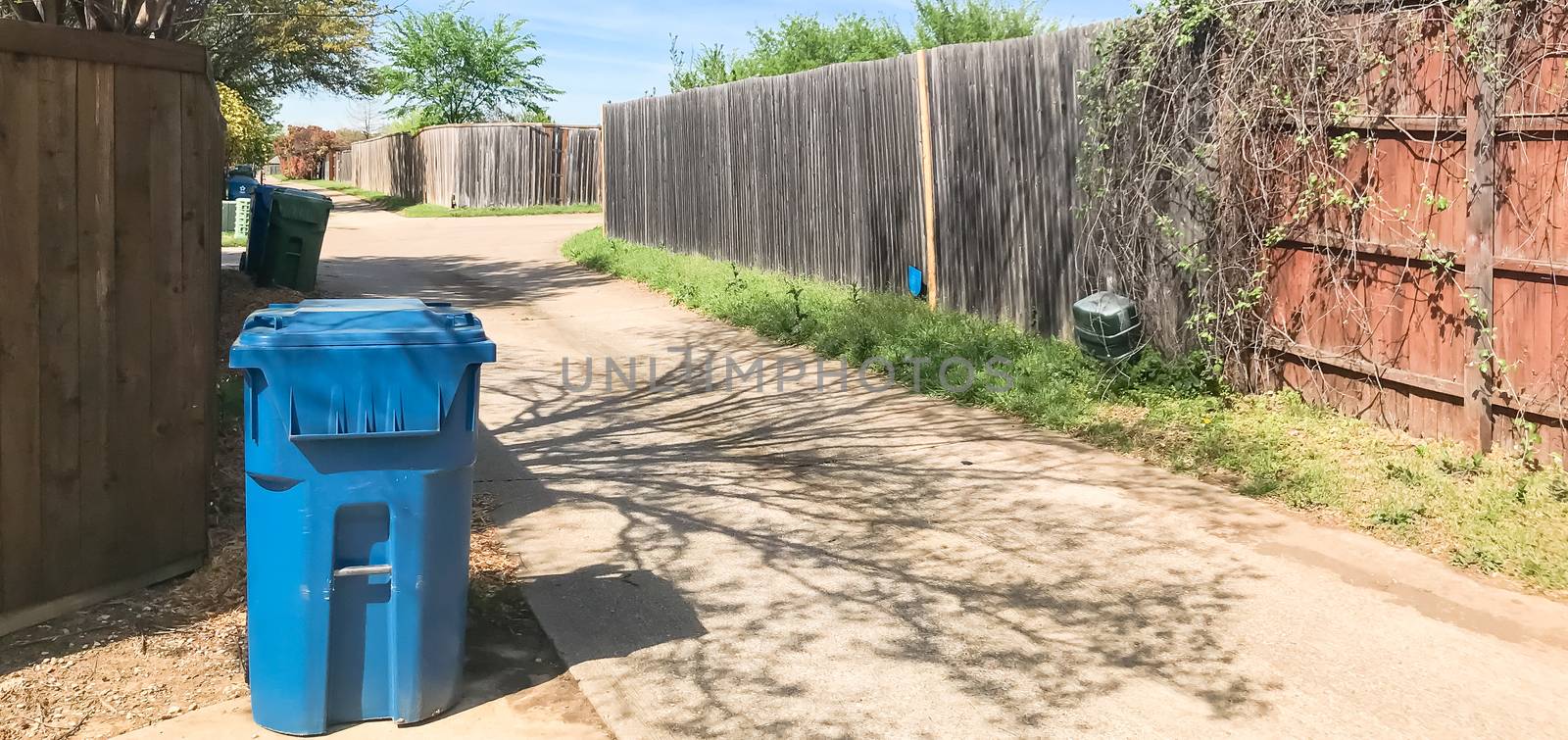 Panorama view empty back alley in residential neighborhood with wooden fence with vines and trash, recycle bin. Quiet suburban area near Dallas, Texas, USA