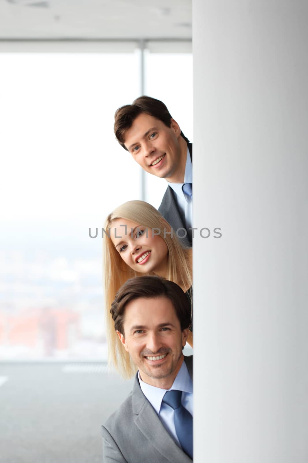 Happy business people looking out from corner in office