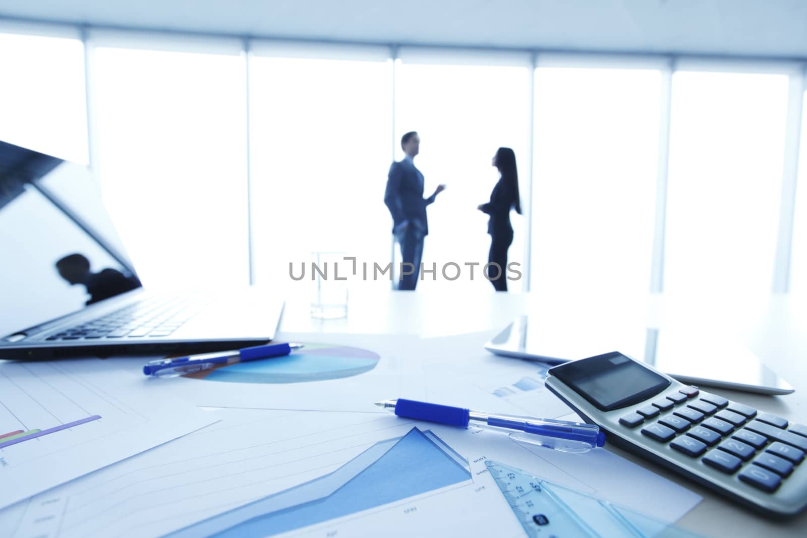 Financial documents , laptop, calculator on table , business team on background