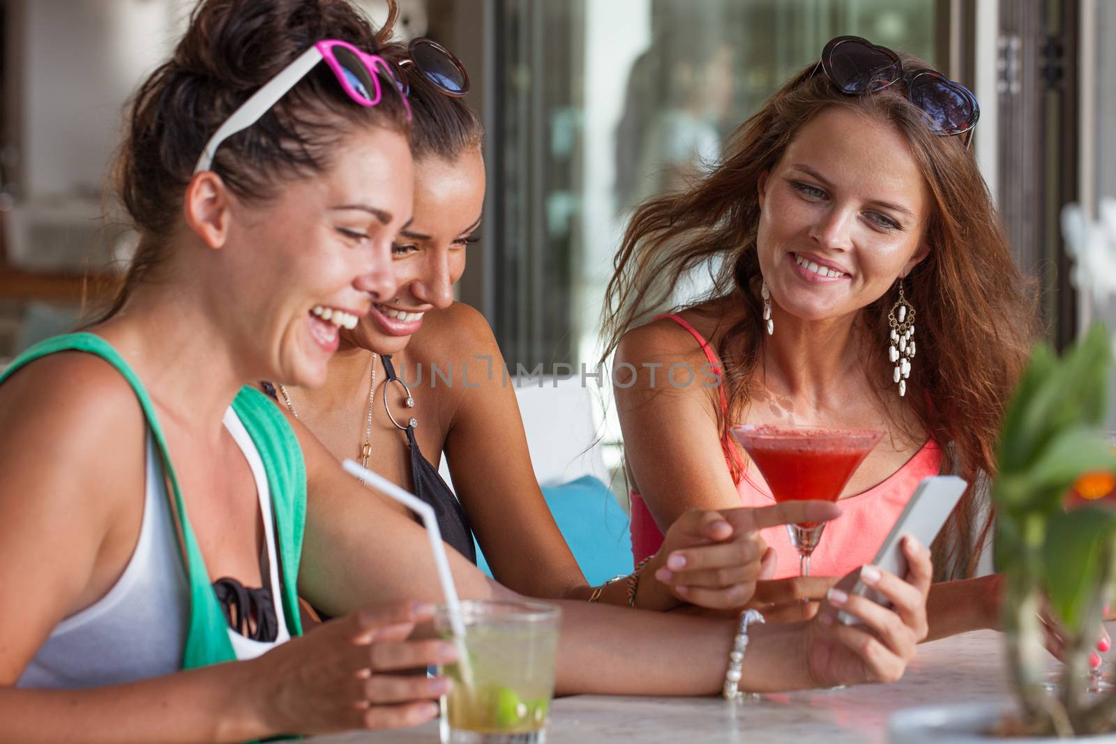 Three friends amazed watching a smart phone sitting in cafe drinking cocktails