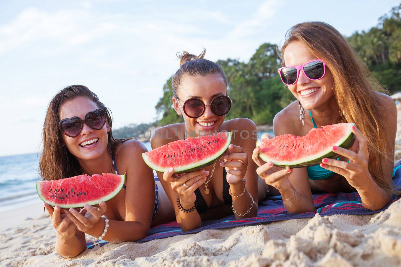 Happy smiling female friends eating watermelon on beach
