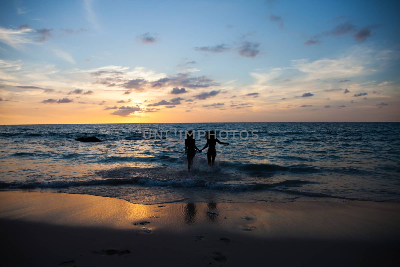 Happy female friends having fun on beach at sunset