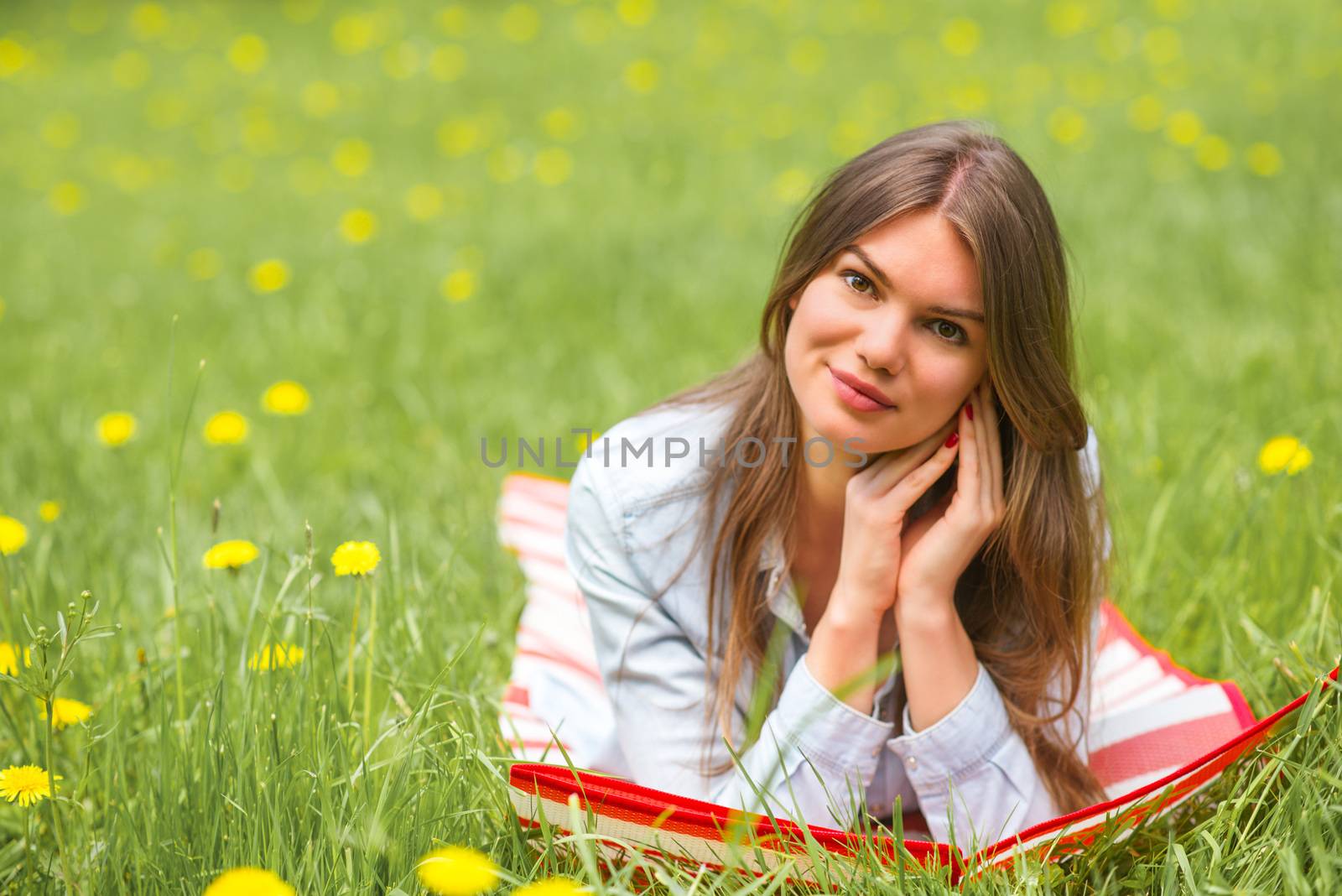 Beautiful young woman laying on grass with dandelion flowers in park