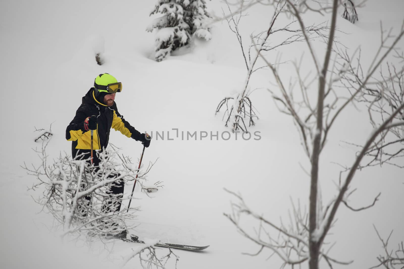 Happy smiling skier walks in the mountains in deep snow after freeride alpine skiing with ski on shoulder