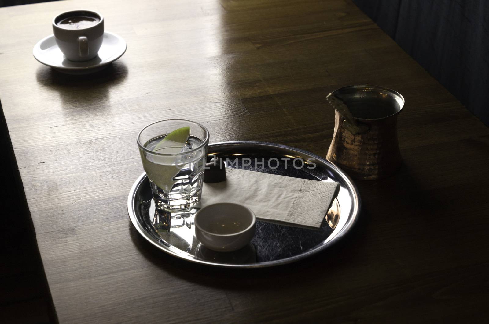 a glass of coffee with coffee pot and chocolate beside a coffee with milk in a white cup placed on a brown table