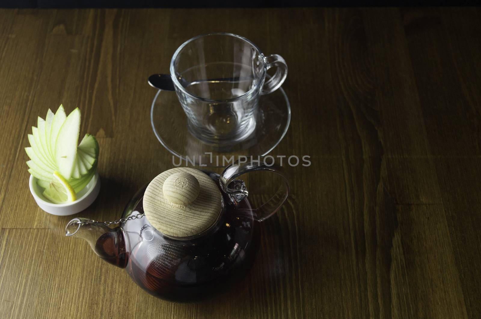 a glass of brewed tea and a glass with lemon in a glass teapot placed on a brown table