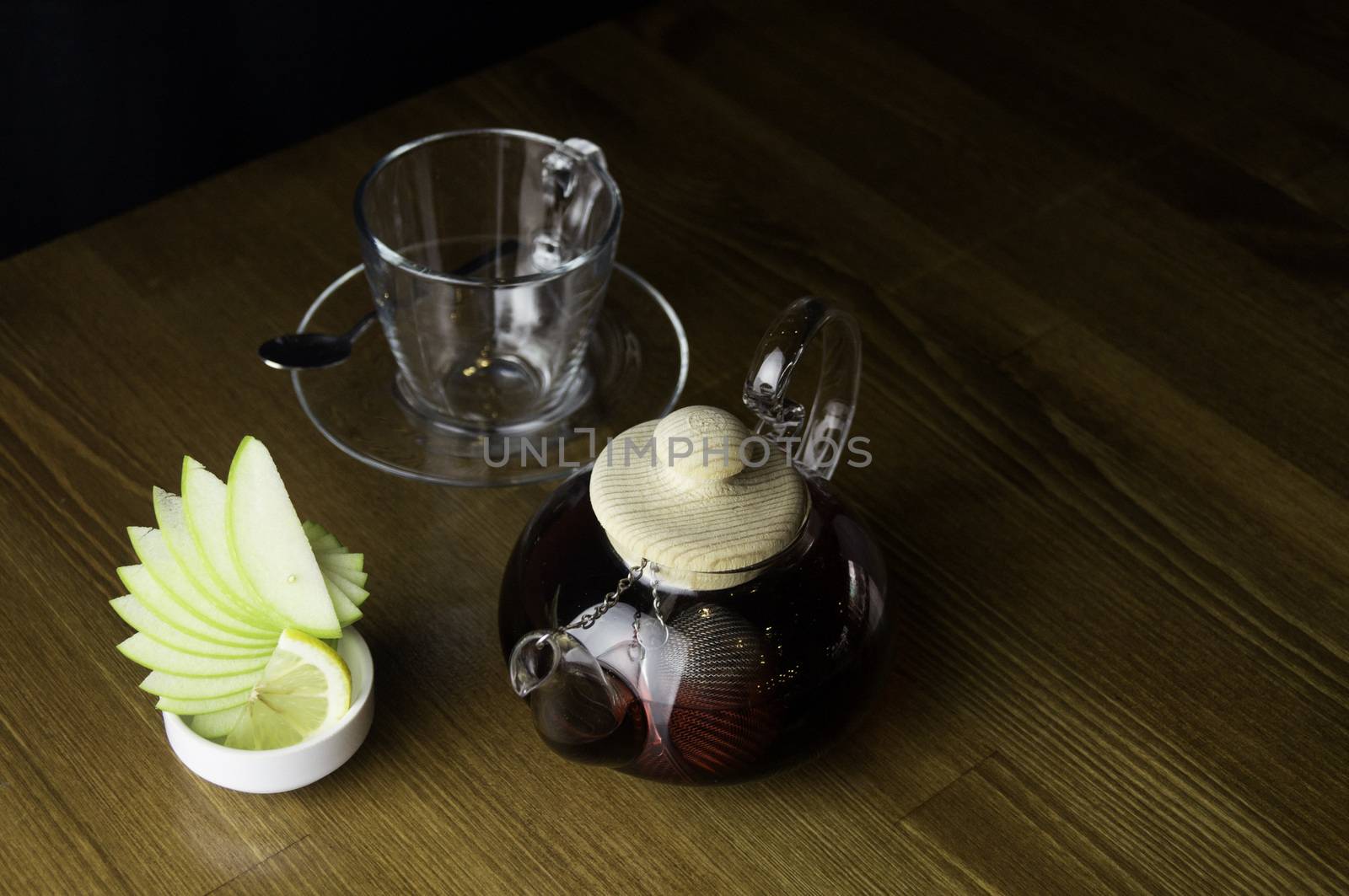 a glass of brewed tea and a glass with lemon in a glass teapot placed on a brown table