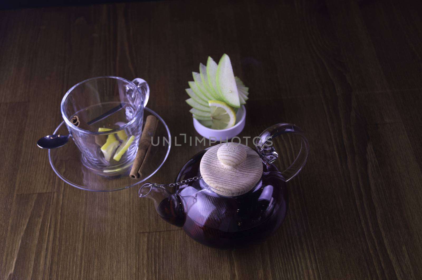 a glass of brewed tea and a glass with lemon in a glass teapot placed on a brown table