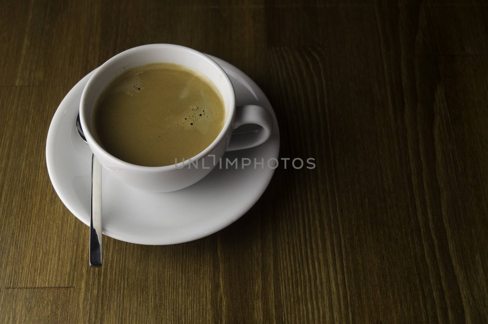 a cup of coffee and spoon placed on a brown table