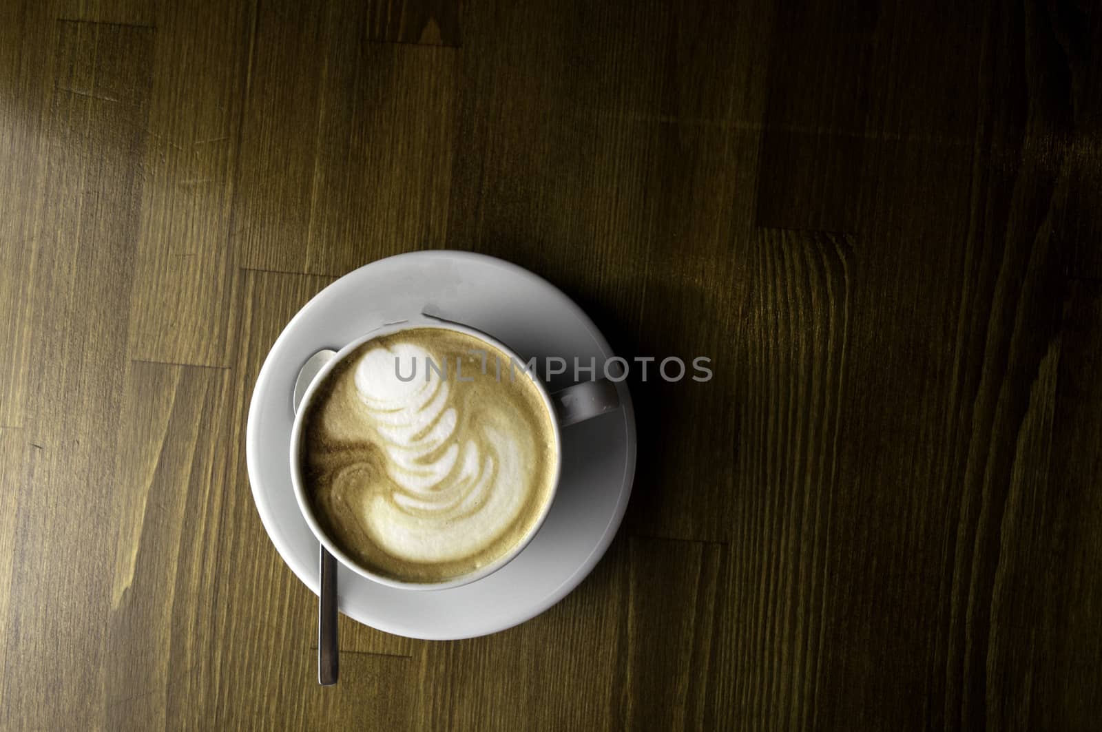 coffee with milk in a white cup on a brown table and spoon to mix