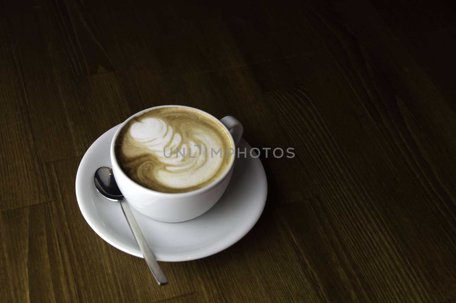 coffee with milk in a white cup on a brown table and spoon to mix