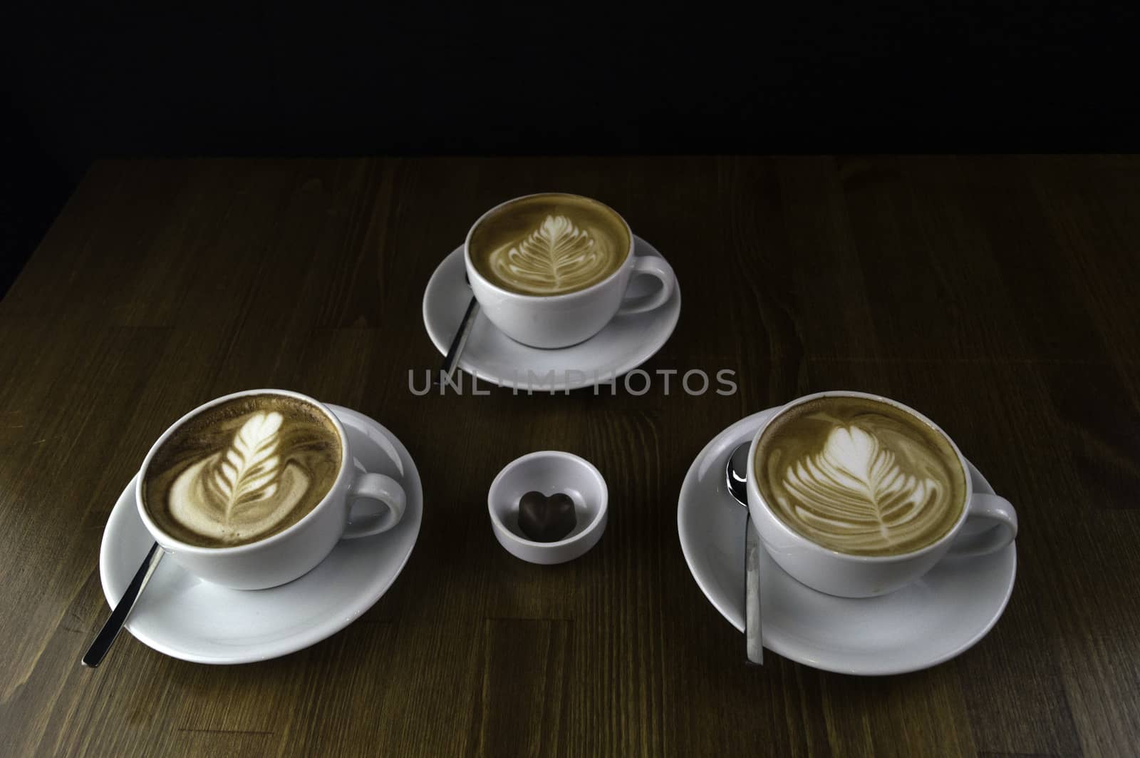 three milk coffee in a white cup on a brown table and chocolate next to it