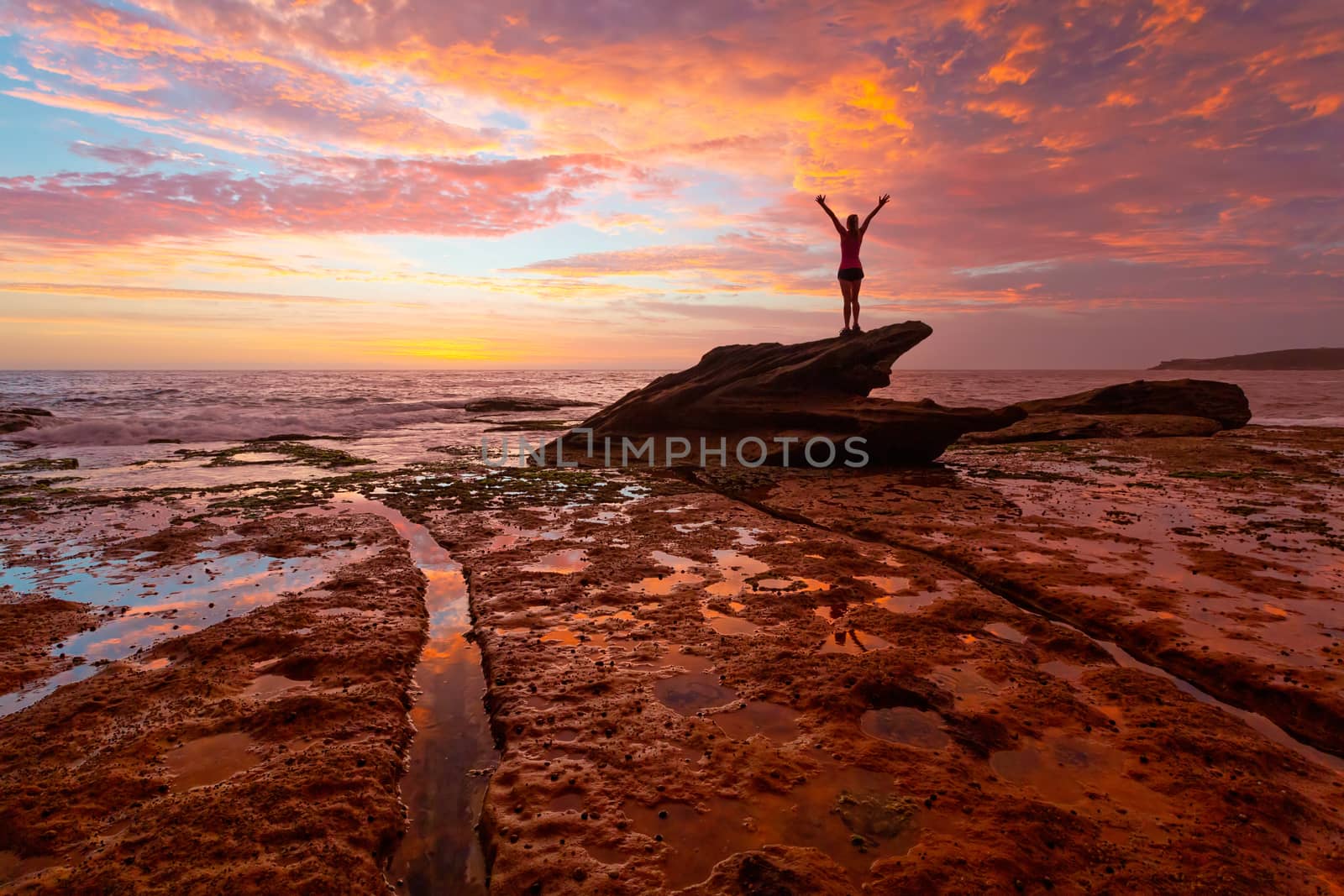 Woman standing on coastal rocks with stunning sunrise and reflec by lovleah