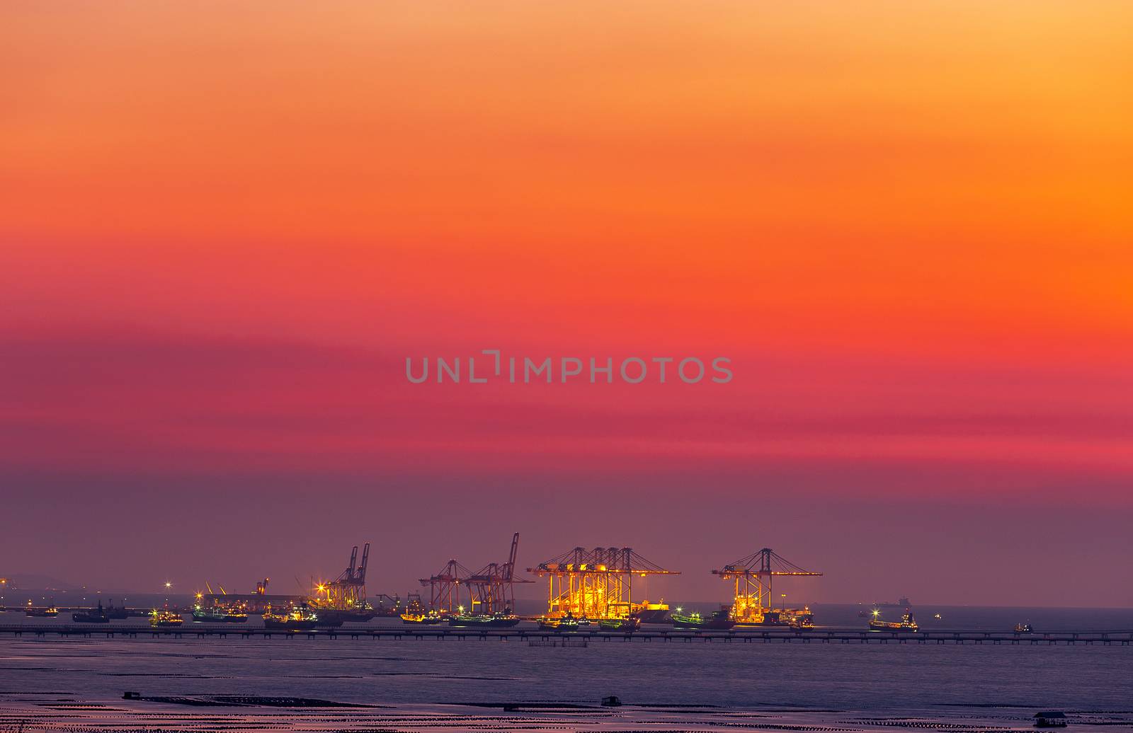 crane at dock of logistic transportation at harbor in sea to deliver chemical and industrial product to industrial plant onshore with beautiful sunset time