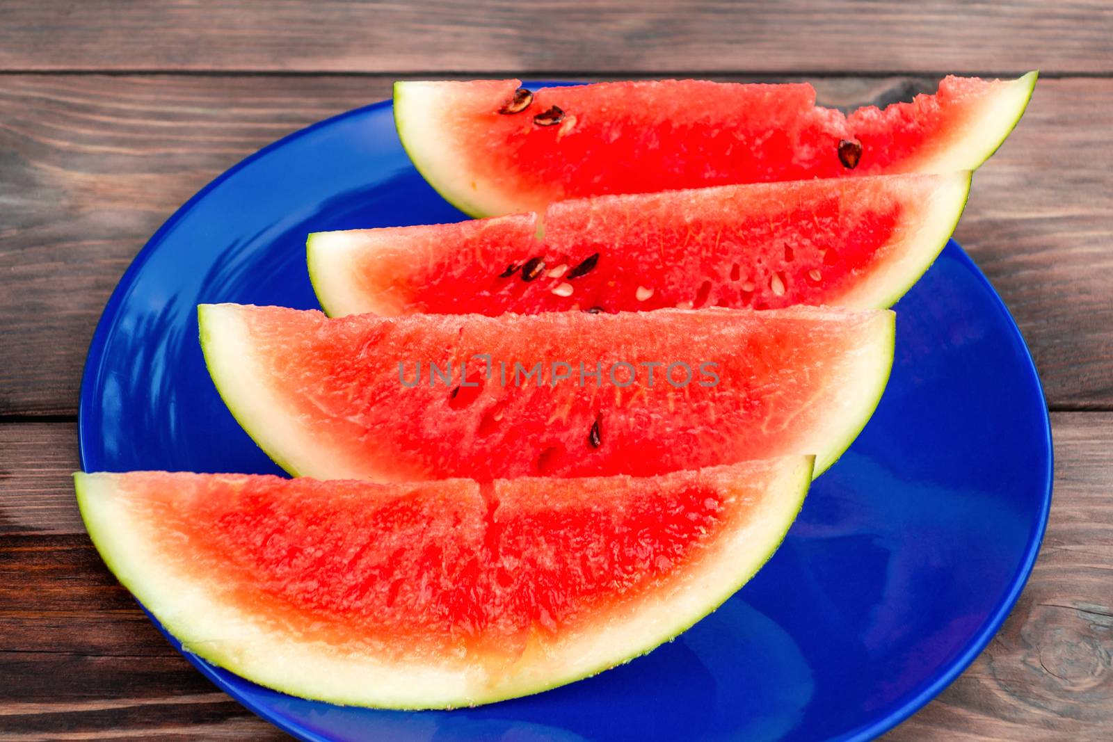 Sliced ripe red watermelon on a blue plate on a wooden table.