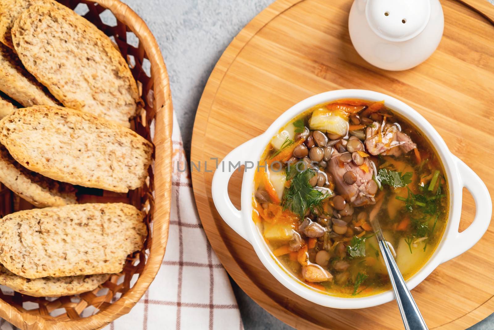 Lentil soup with chicken in a white bowl on a wooden board, top view.