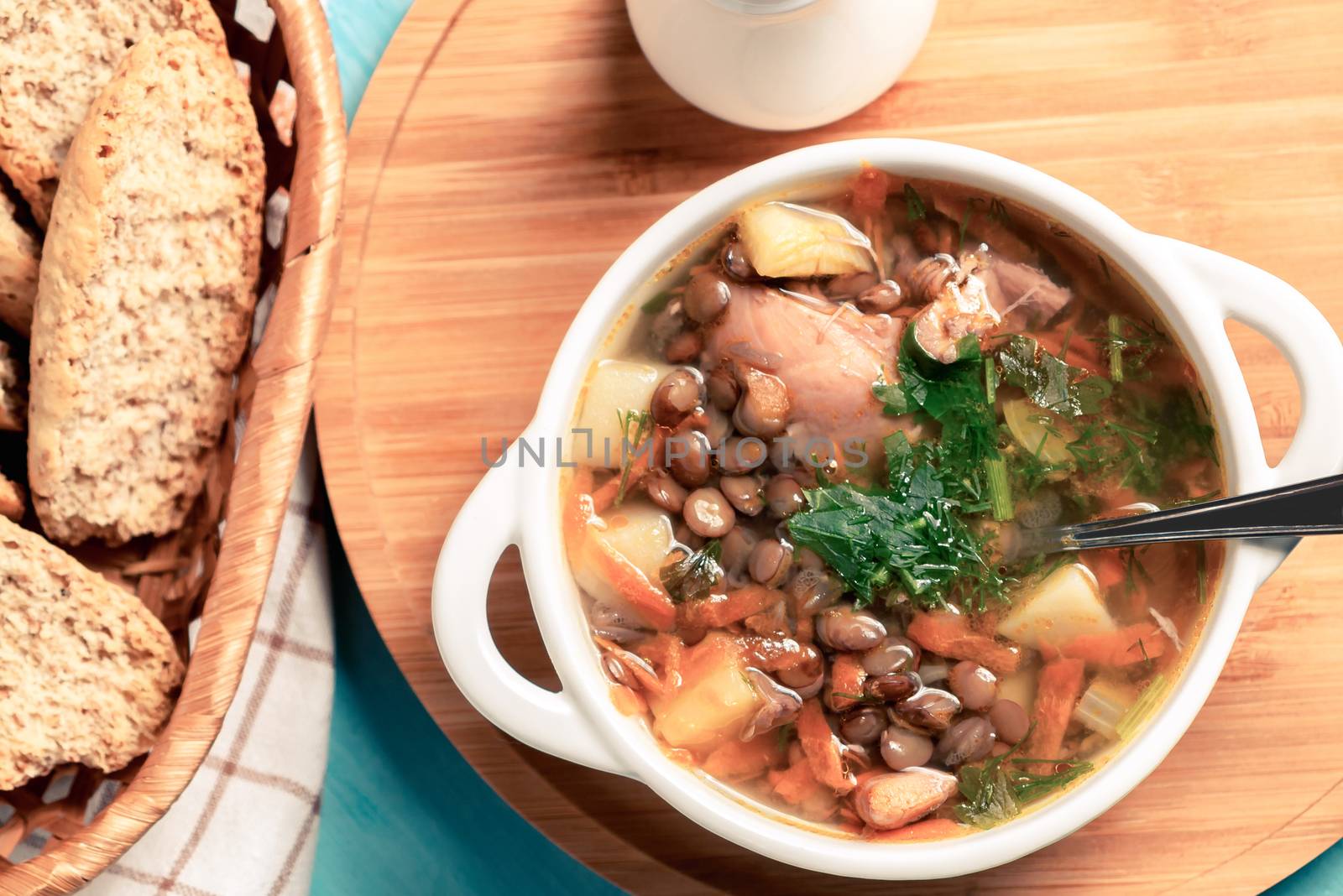 Lentil soup with chicken in a white bowl on a wooden board on a blue table, top view by galsand