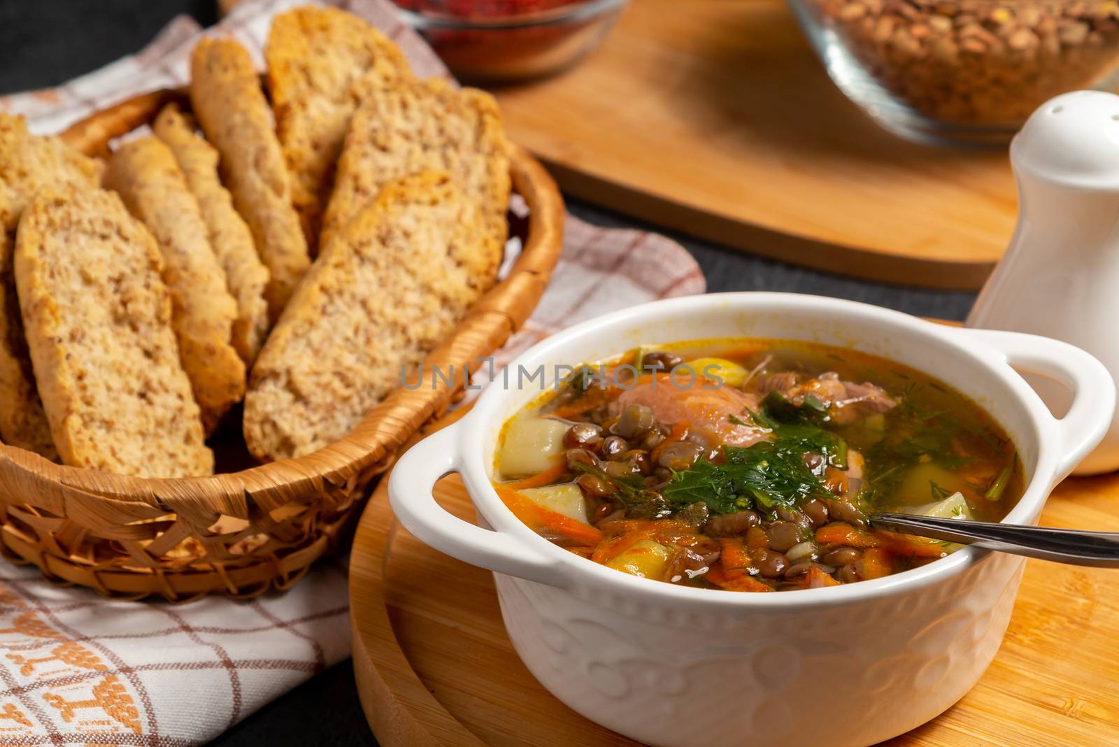Lentil soup with chicken in a white bowl on a wooden board on a black table and ingredients.