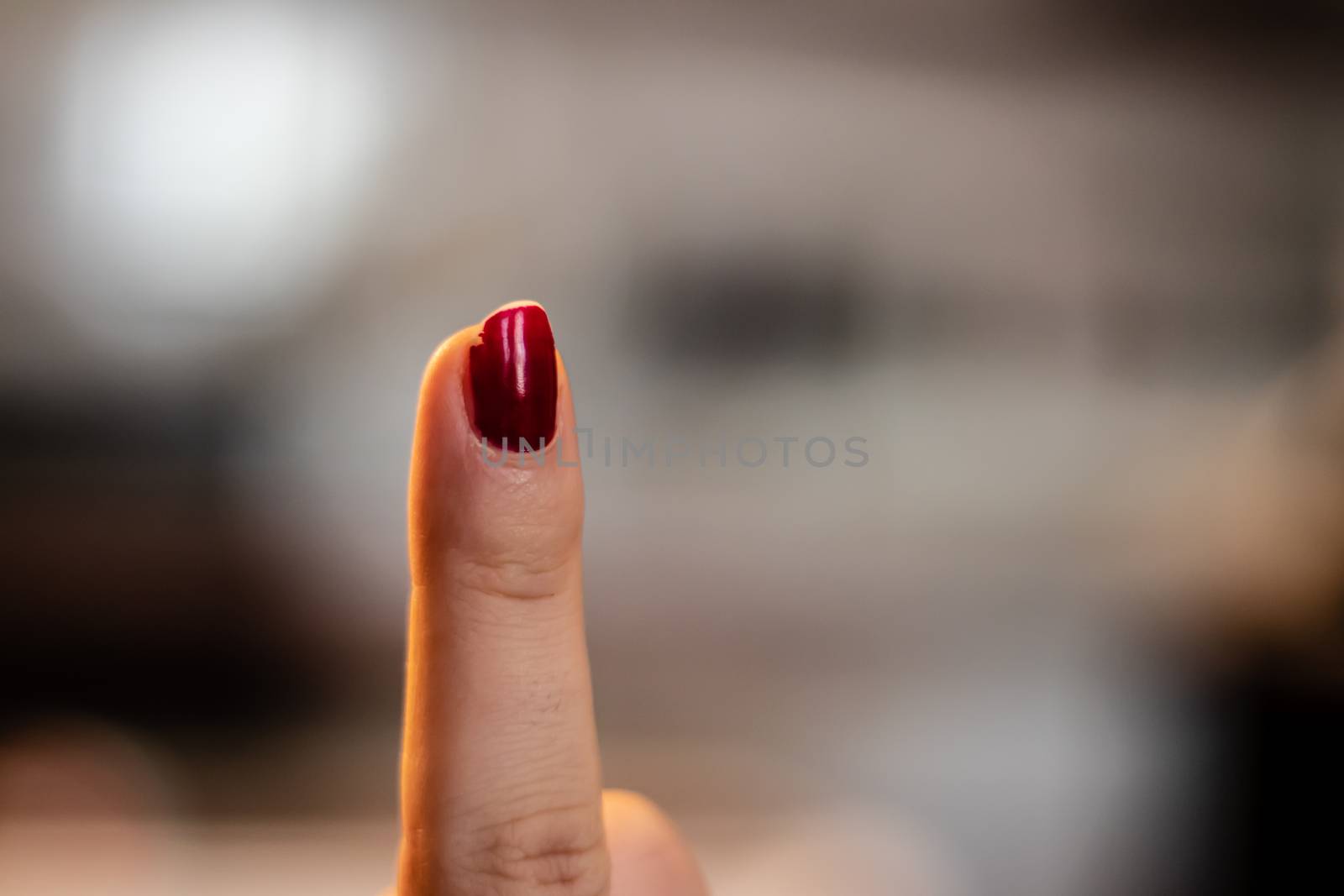 a closeup shoot to woman finger with red nail polish, background is blurry. finger pointing up.