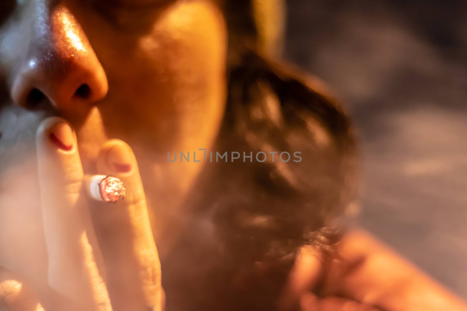 a girl smoking a cigarette with rubbed out red nail polish. background is blurry.