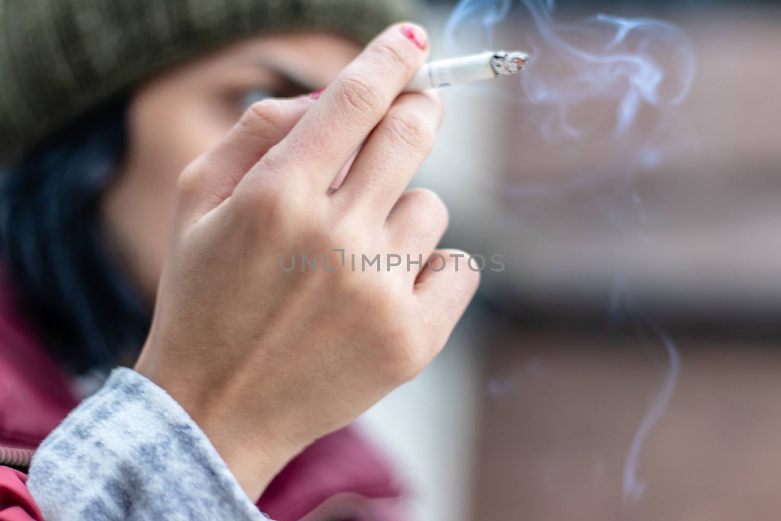 a side shoot of girl smoking a cigarette with rubbed out red nail polish. background is blurry.