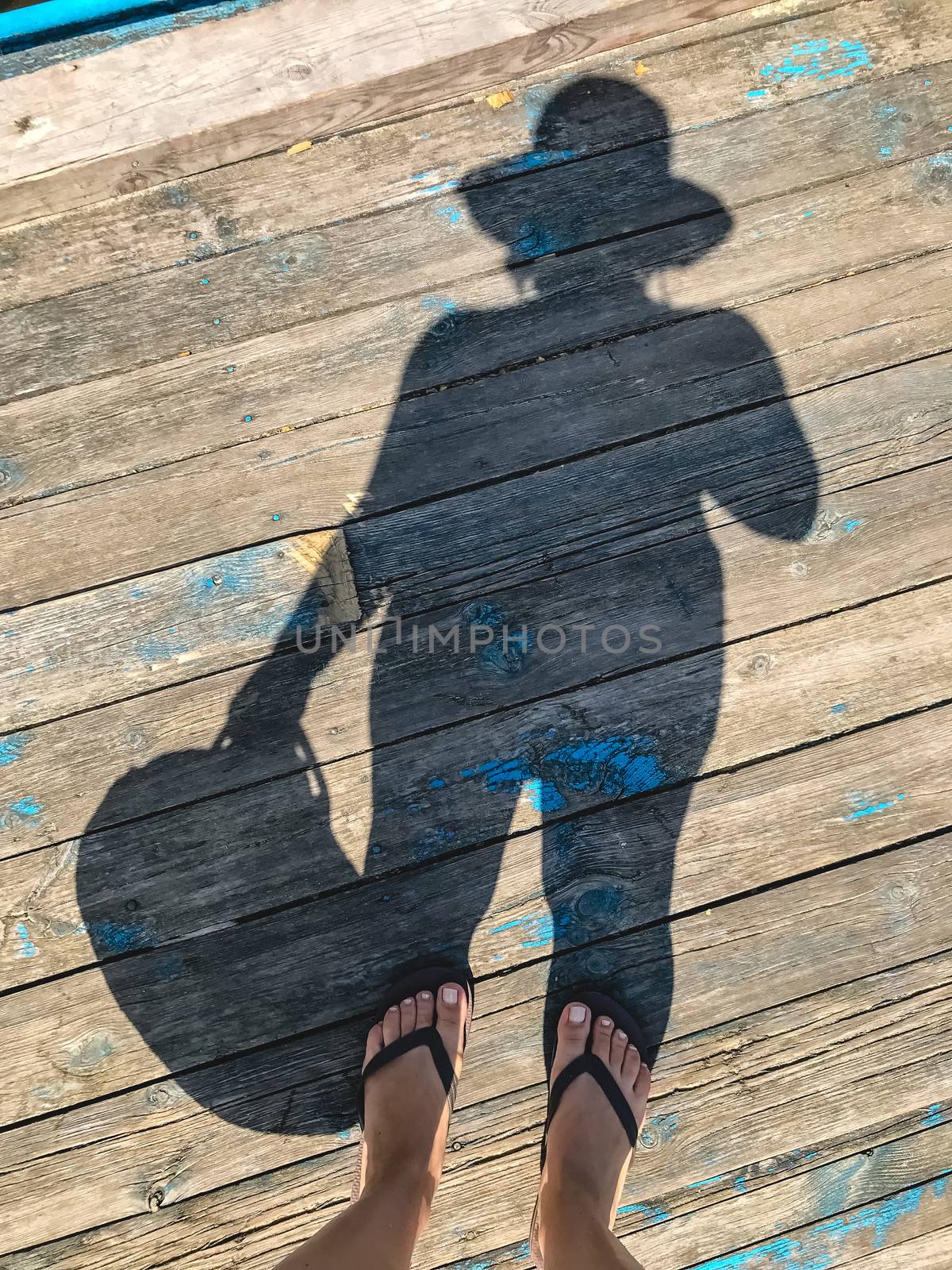Top view, photo of bare feet and a pair of shadows on a wooden old floor. Photos on vacation, beach, summer.