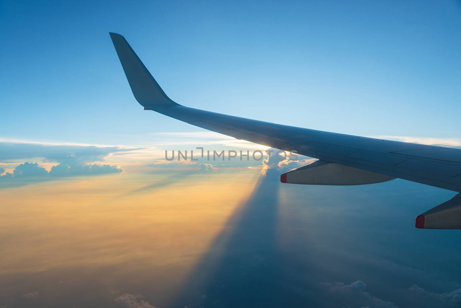 View of airplane wing and sunset sky. Plane in flight, clouds project long shadows.