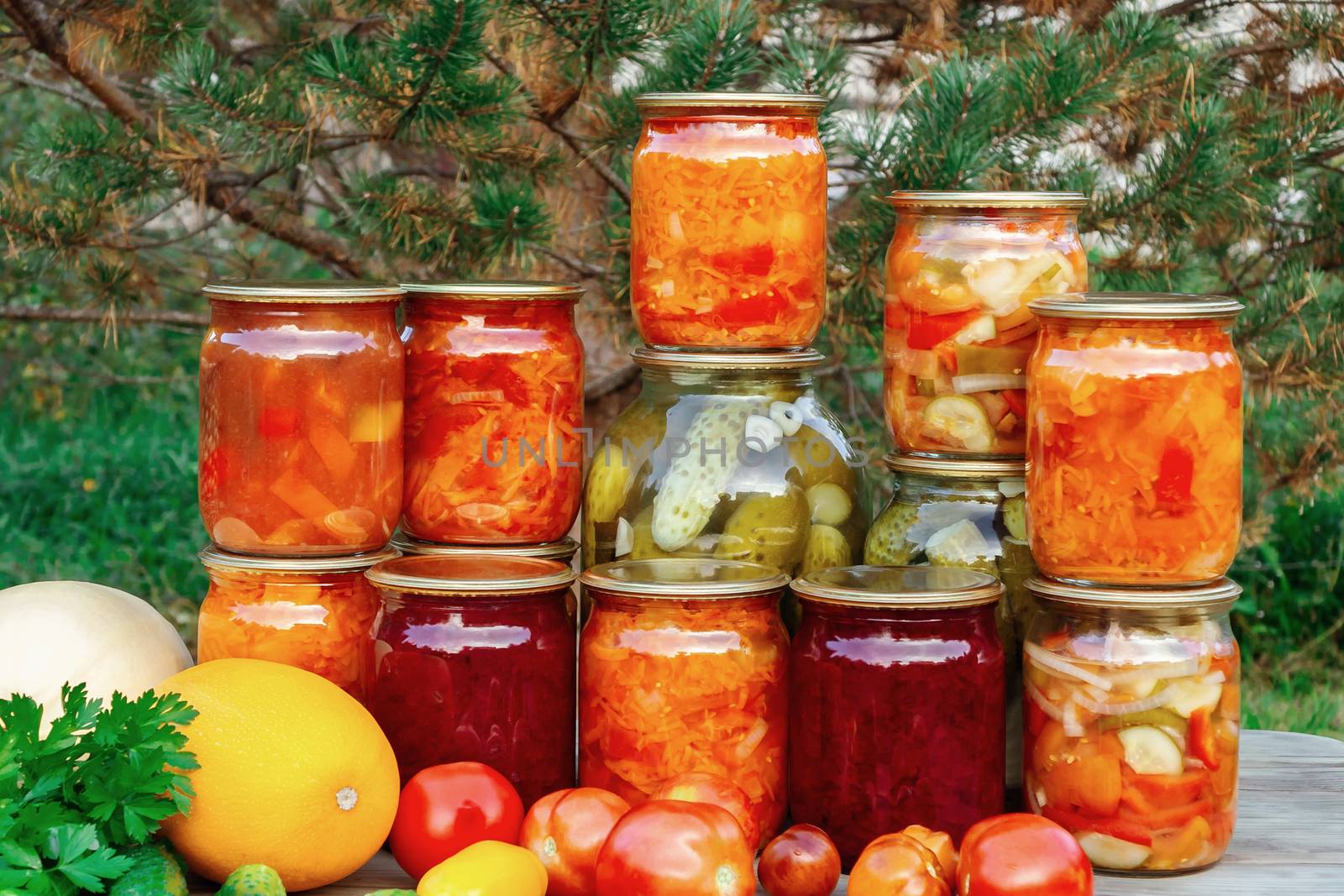 Several homemade jars of canned vegetables and fresh vegetables on a wooden table - image.