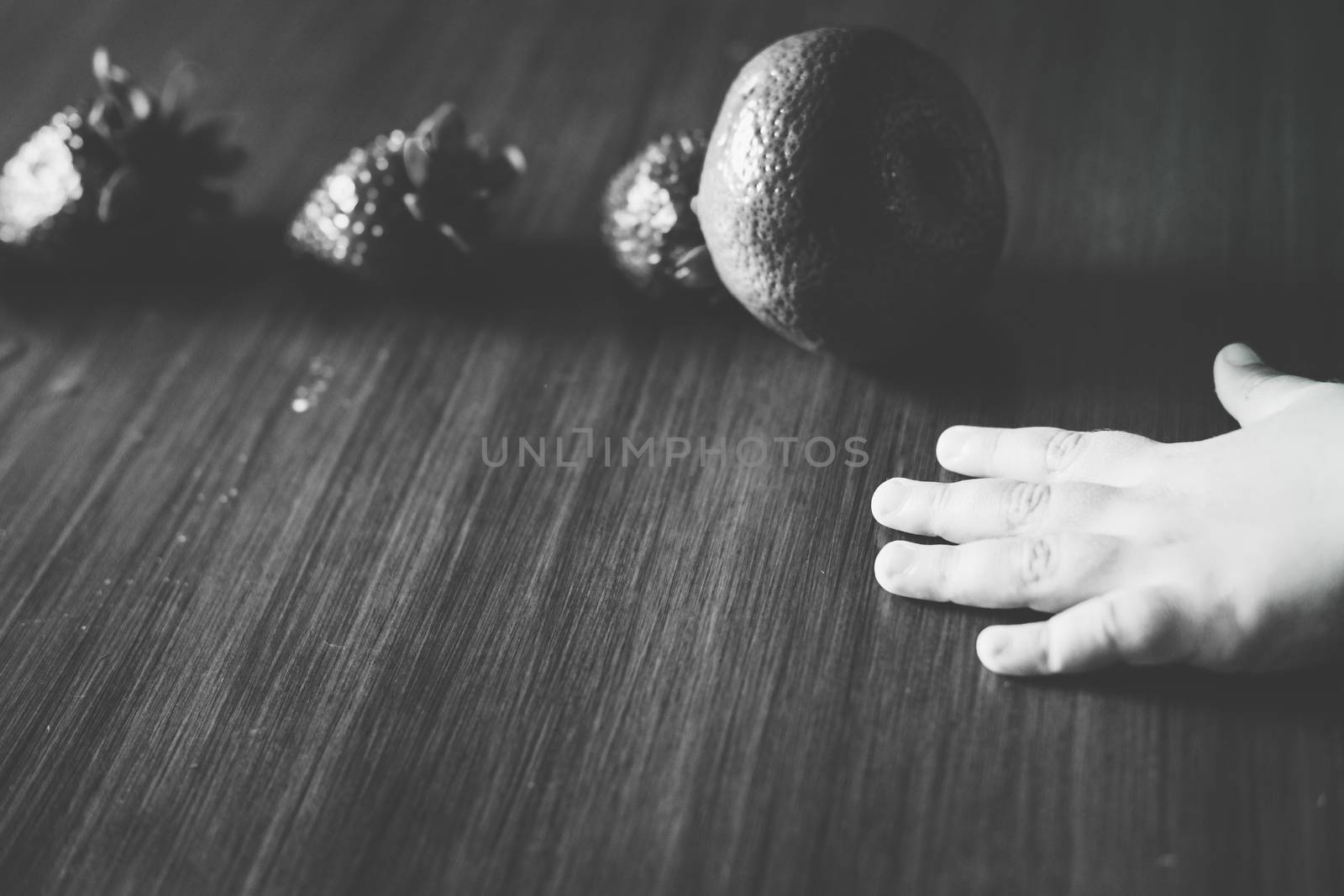 Light hand in contrast with dark straeberries and a tangerine forming a line on the table