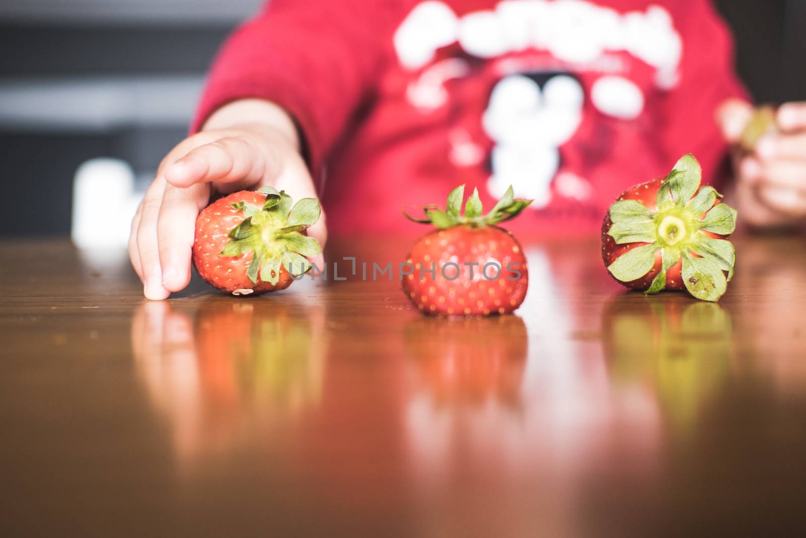 One of the strawberries forming a line on the table is being grabbed by a kid