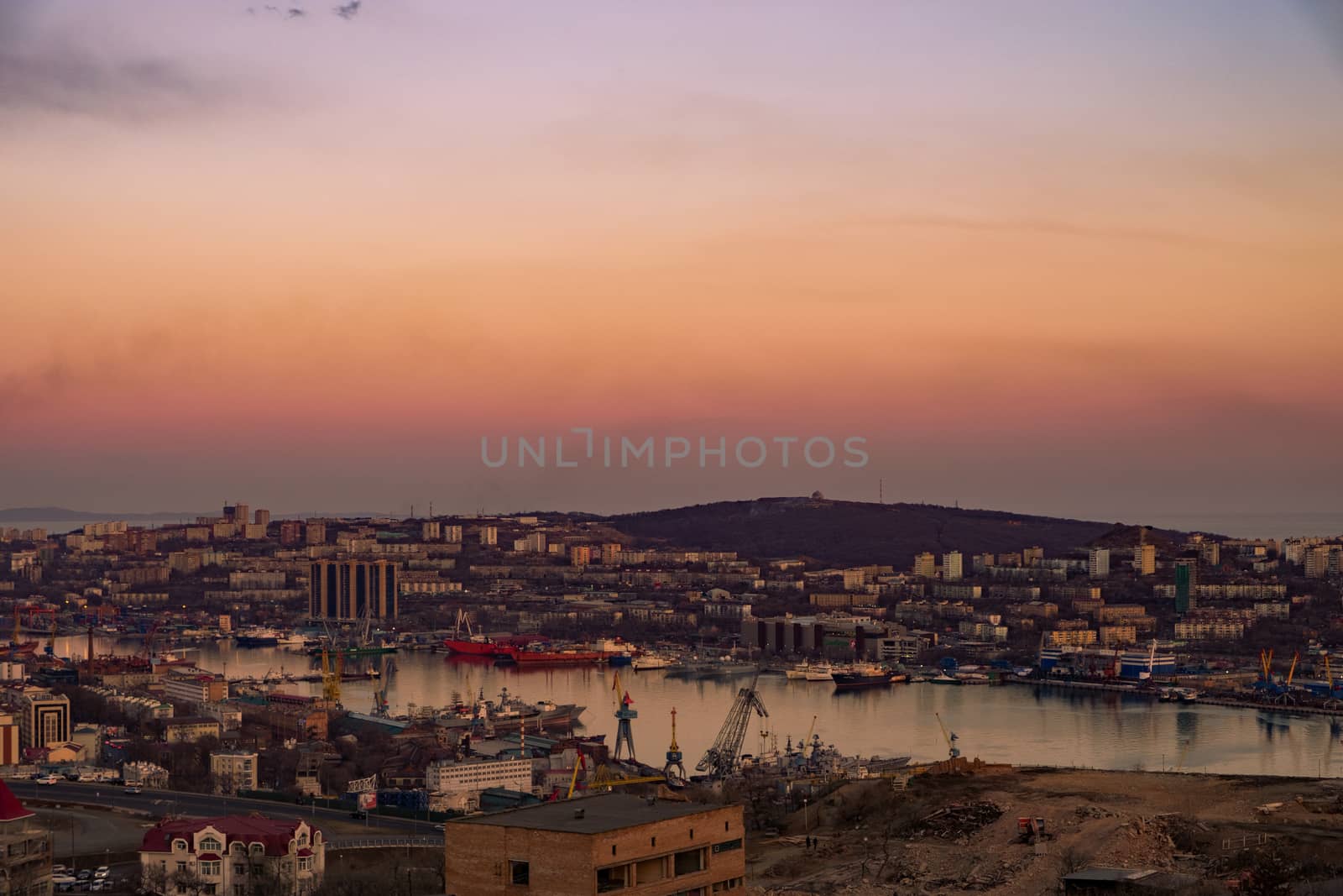 View of the city of Vladivostok from the hill eagle's nest . Sunset. The sky is orange and pink. Sea and city at sunset.