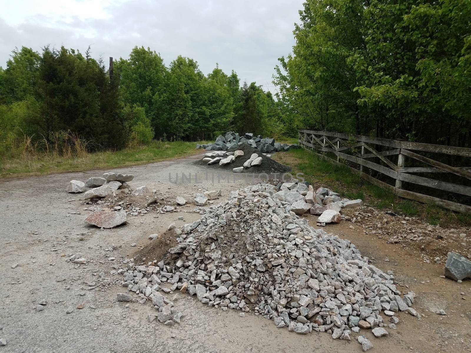 asphalt street or road with piles of grey rocks or stones and trees