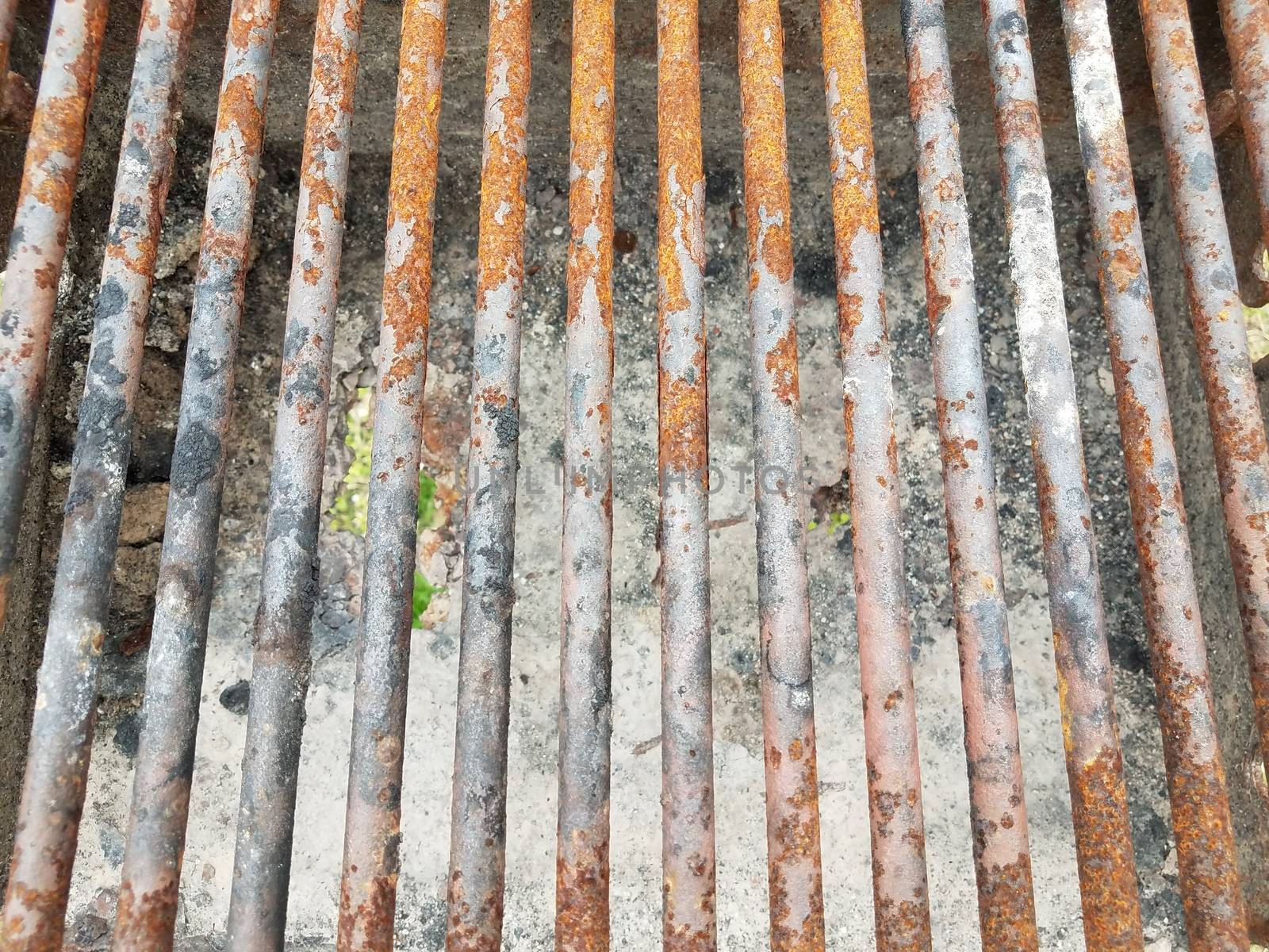 weathered and brown rusted metal bars on barbecue grill with soot and a hole