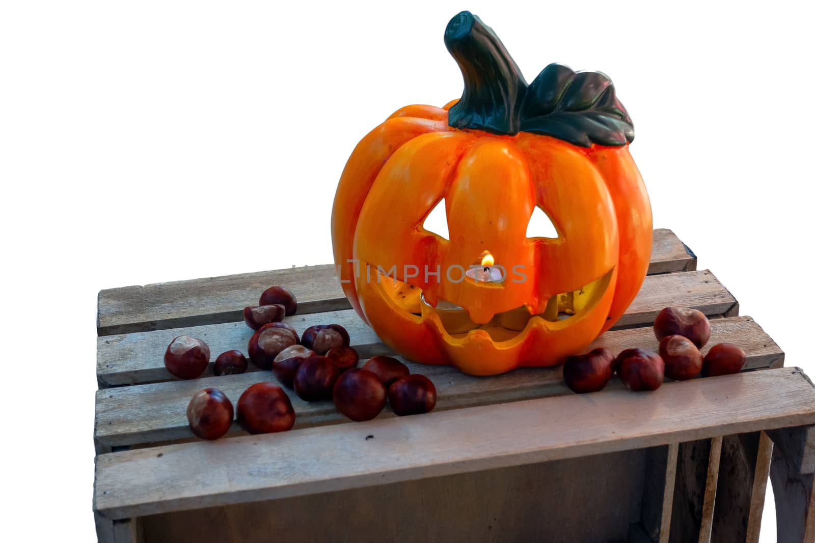 Halloween Pumpkin with Chestnuts Decoration on wooden box, autumn holiday concept,, burning candle seen through nose, candle flickering in wind, isolated on white