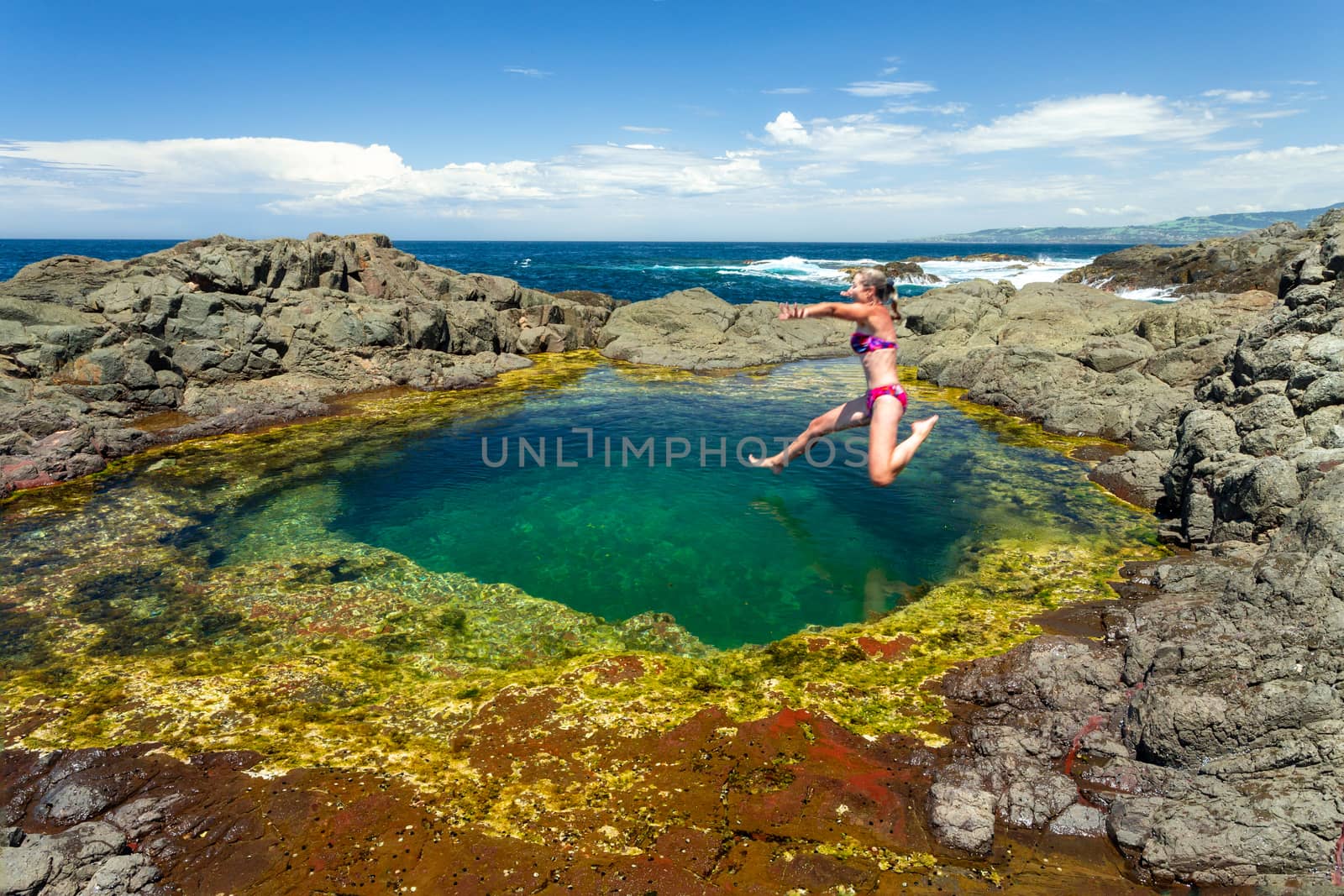 Woman jumping mid air into a beautiful clean rock pool on the coastal foreshore by lovleah