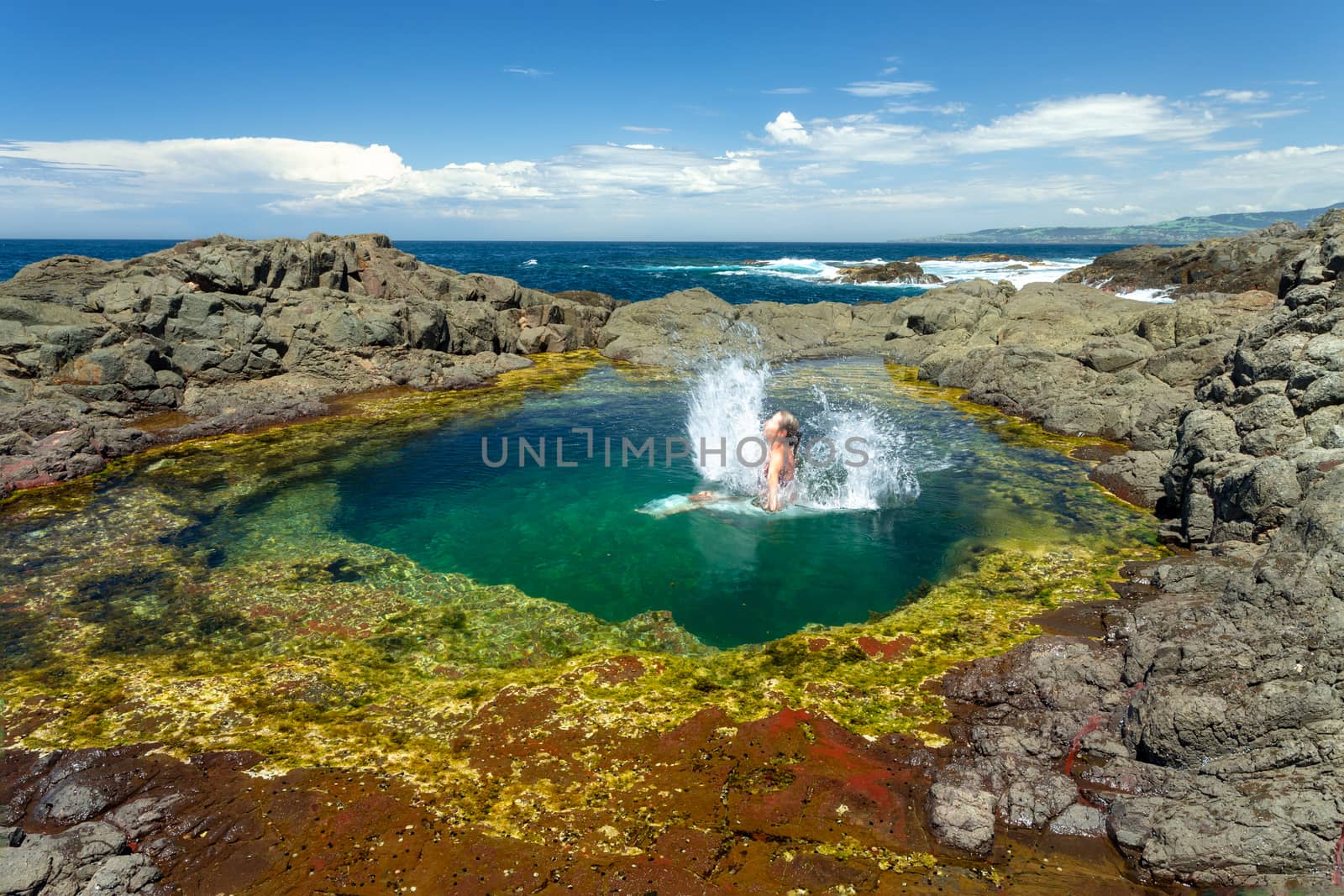 Woman making splash jumping into beautiful natural tidal  rock pool by lovleah