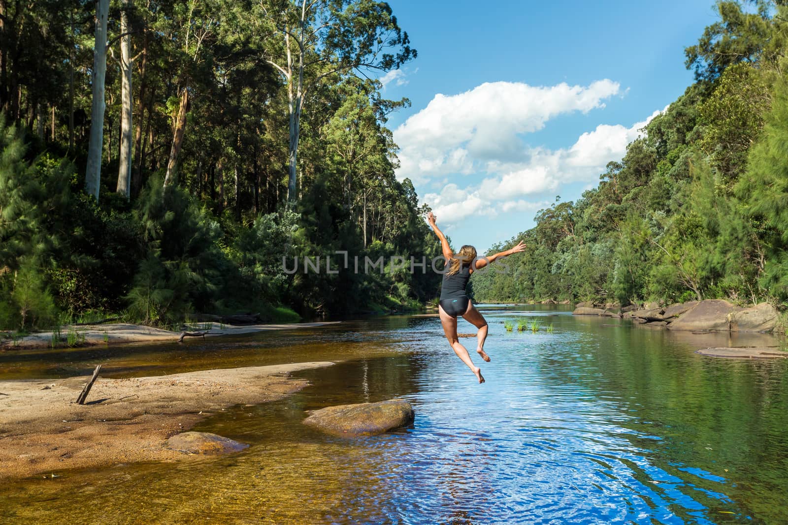 Active exuberant woman jumping into river in remote bushland paradise.  Blue Mountains Australia