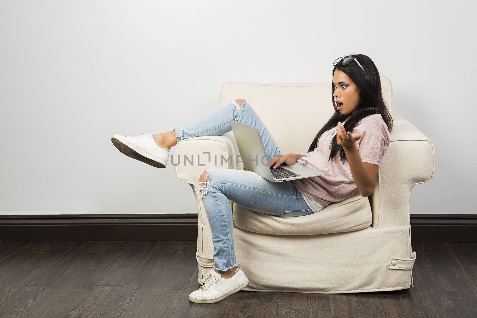 young woman, sitting on a couch, working on a laptop, with an expression of frustration